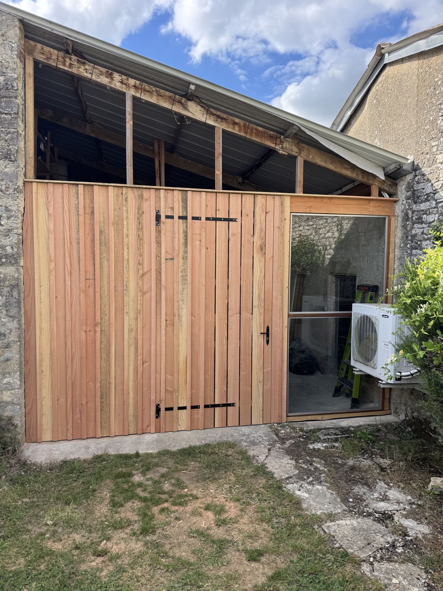Façade en bois avec porte de grange à un vantail et partie vitrée.