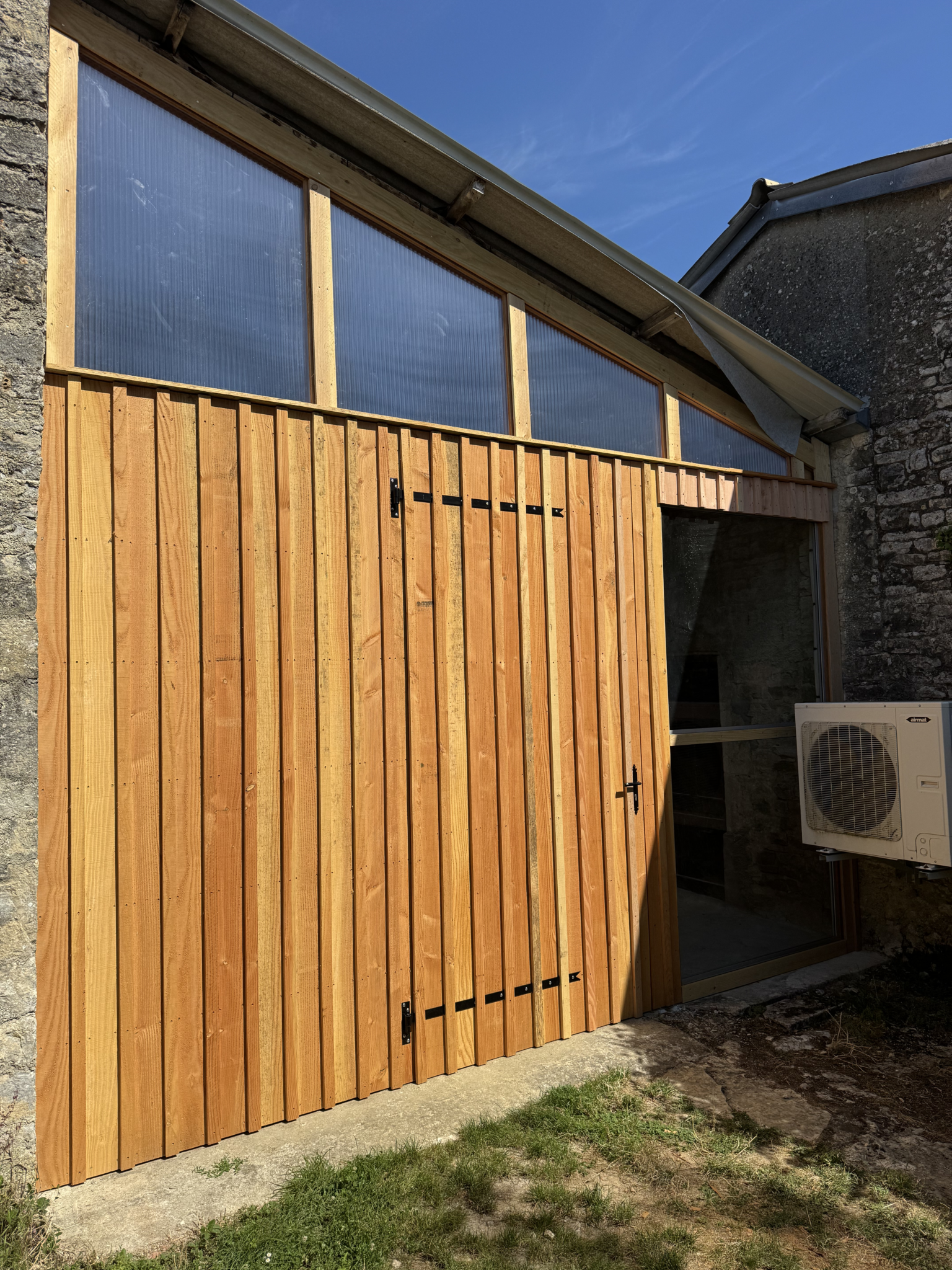Façade de grange rénovée en bois avec porte battante et panneaux translucides