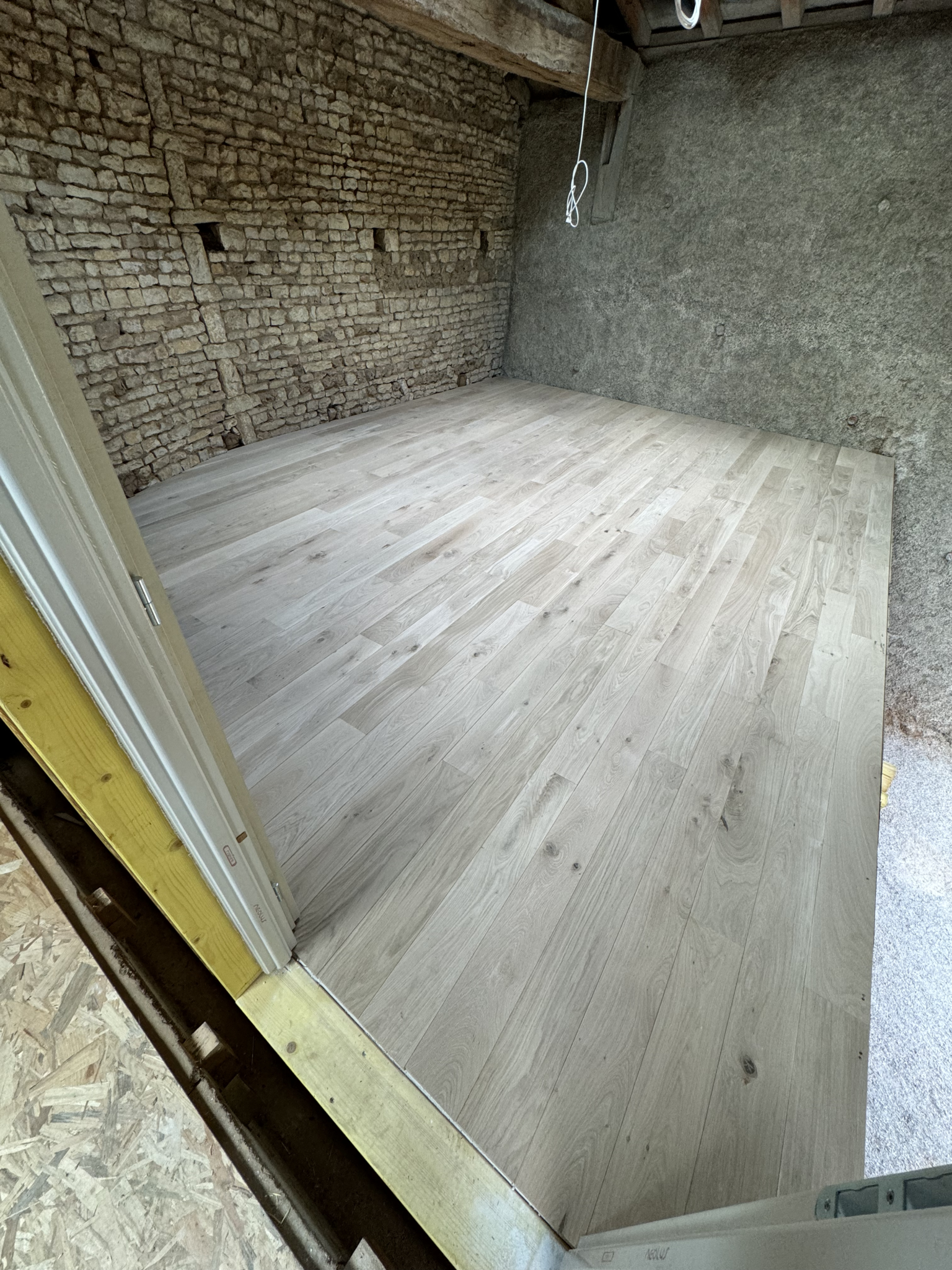 Parquet massif en chêne posé dans une pièce aux murs en pierre à Brux