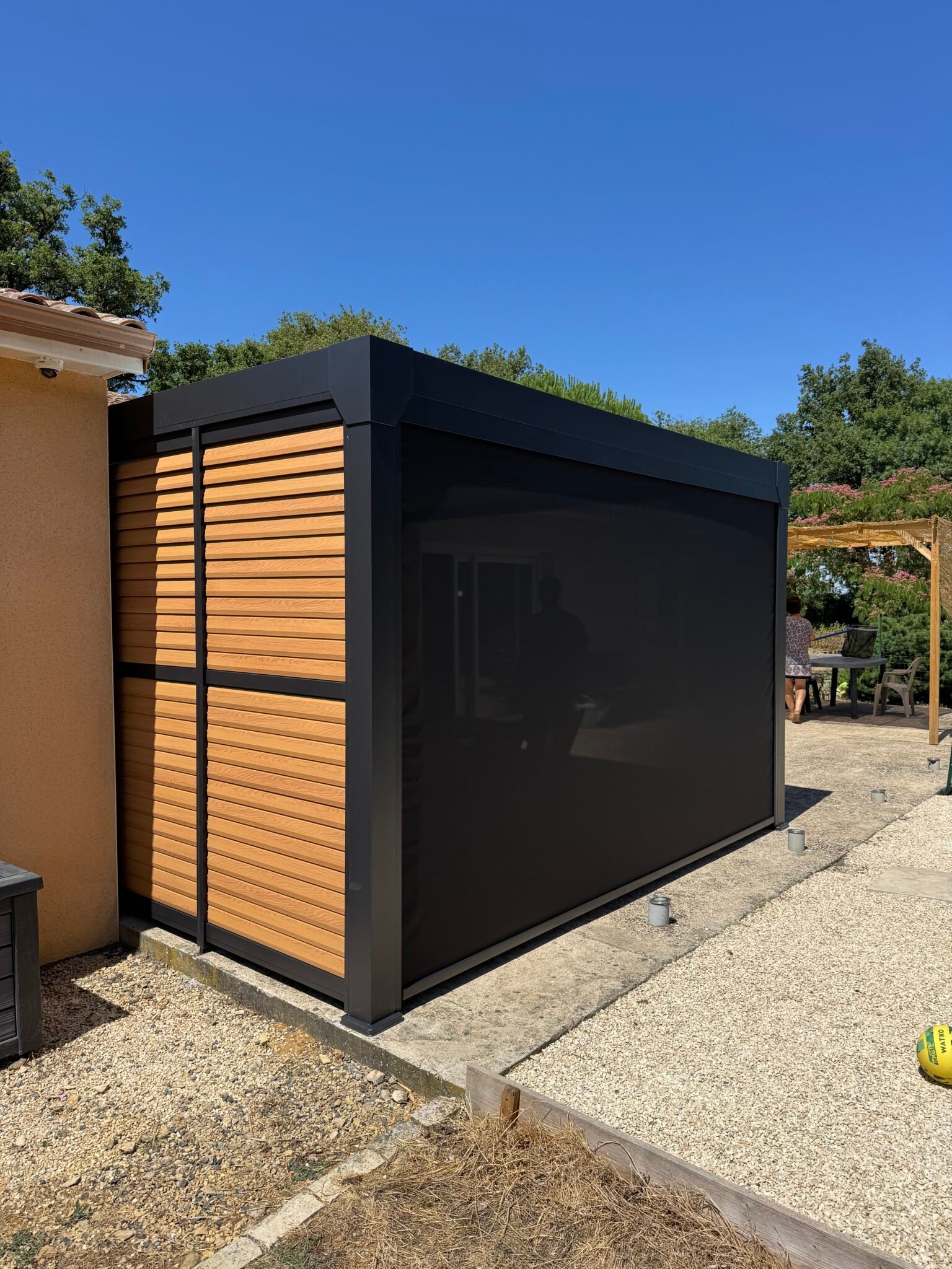 Pergola bioclimatique en aluminium gris anthracite avec claustra effet bois et store screen fermé