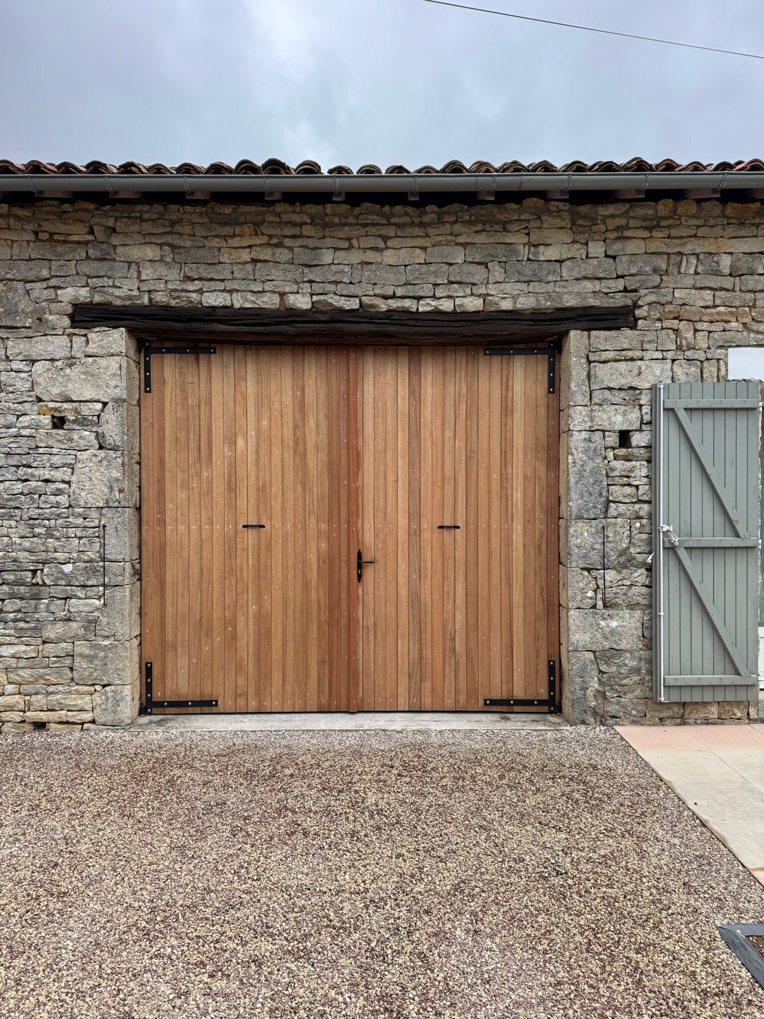 Porte de grange en bois exotique fermée sur une façade en pierre à Brux