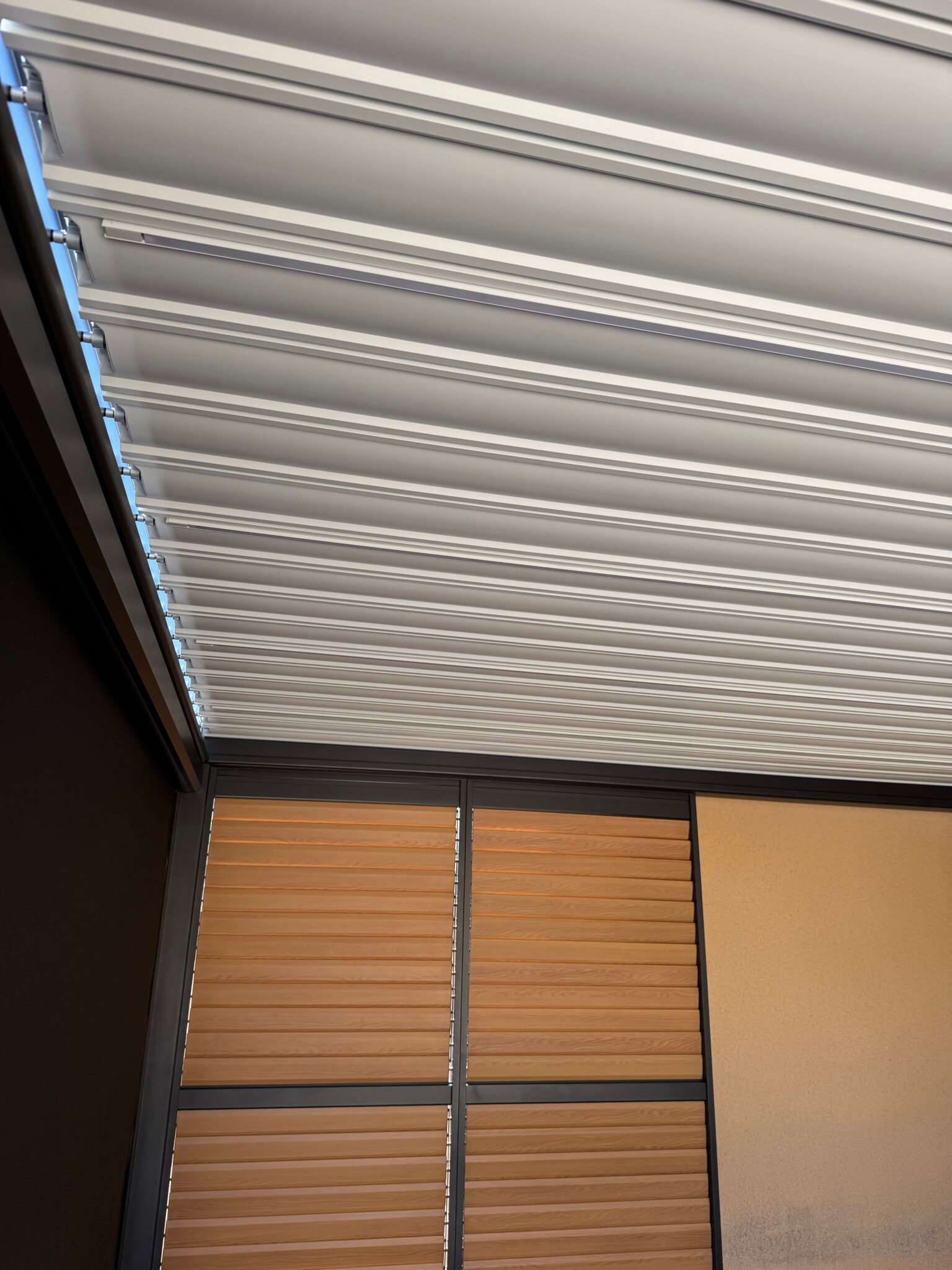 Vue intérieure d’une pergola bioclimatique avec lames orientables blanches et claustra effet bois